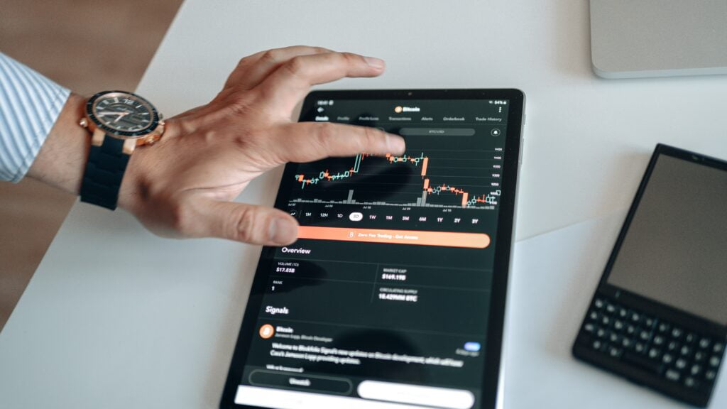 A hand on a forex chart showing in a tablet on a table.